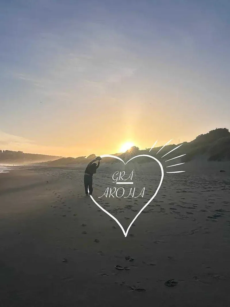A stretch on a beach at sunset, with a heart drawn around it and the words Grá and Aroha